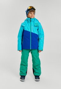 Schneejacke in Hellblau und Marineblau, kombiniert mit grüner Hose. Verfügt über mehrere Reißverschlüsse, verstellbaren Kragen und eine Skibrille auf dem Kopf.