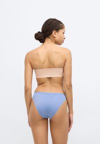 Ελαφρώς δομημένο τοπ μπαντό σε μπεζ απόχρωση σε συνδυασμό με μπικίνι σλιπ χαμηλής μέσης σε μπλε, με λείο ύφασμα, καθαρές γραμμές και ελάχιστο μεταλλικό εξάρτημα.