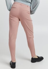Světle růžové slim kalhoty vyrobené z hladké látky, s dvěma zadními kapsami a elegantním designem, kombinované s černými plochými botami.