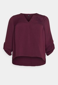 Blouse bordeaux avec un décolleté en V, des manches retroussées 3/4 et un tissu texturé. Présente un ourlet légèrement incurvé pour un ajustement décontracté.