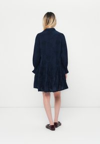 Navy blue dress with floral embroidery, long sleeves, and a tiered skirt. Soft fabric texture, collared design, and a fitted bodice.