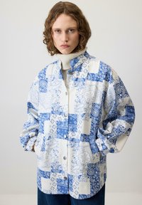 Jachetă cu un model albastru și alb, cu m�âneci lungi, având un închidere cu nasturi și buzunare laterale, confecționată dintr-un material ușor.