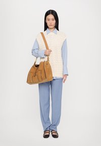 Bež pleteni prsluk preko svijetloplavog prugastog košulje, uparen sa svijetloplavim hlačama i smeškim torbom. Smeškeni cipele završavaju ovu kombinaciju.