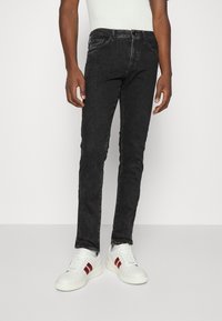 Svarta denimjeans med smal passform, femficksdesign och subtilt blekt mönster, kombinerat med vita sneakers med röda detaljer.