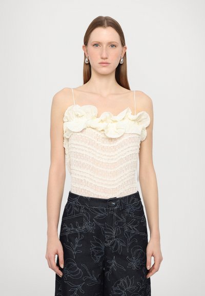 Hvid tanktop med rynkede blomsterdetaljer ved halsudskæringen, tekstiler med stribet struktur. Sammen med mørke denimbukser med blomsterprint.