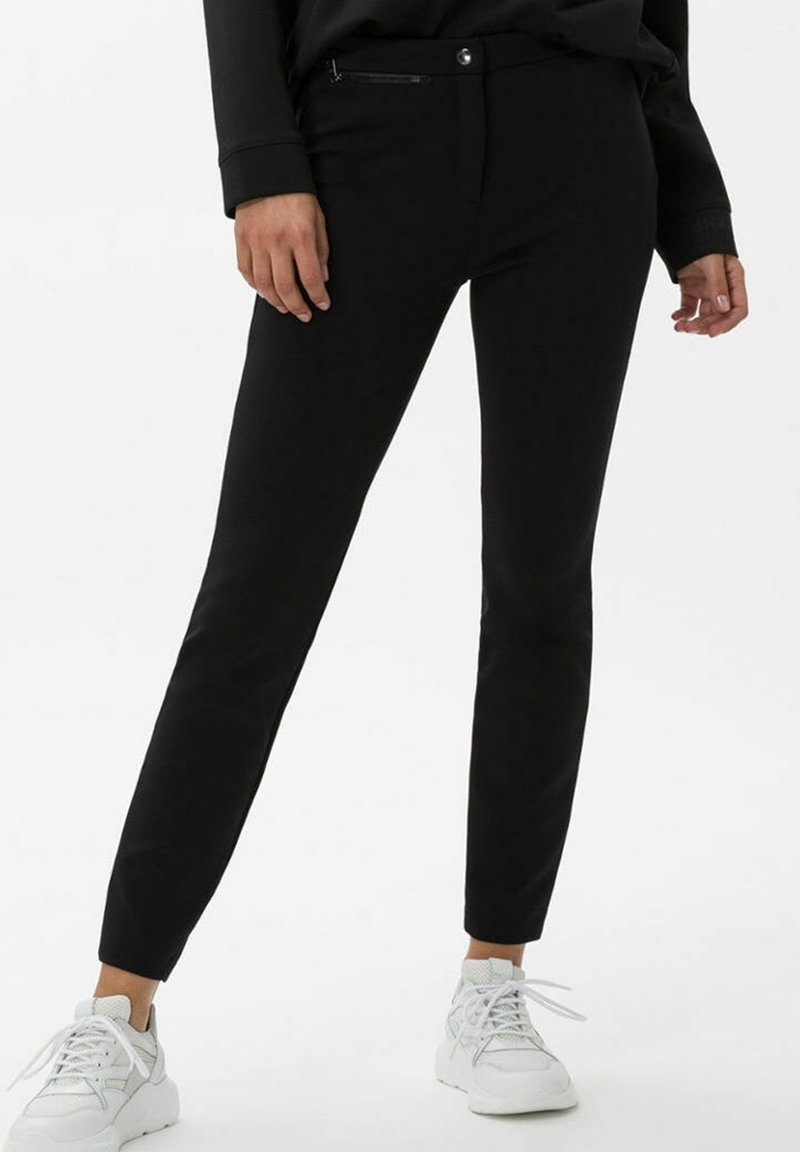 Black pants made of smooth fabric with a slim fit, featuring a zippered pocket, button closure, and ankle-length design, paired with white sneakers.