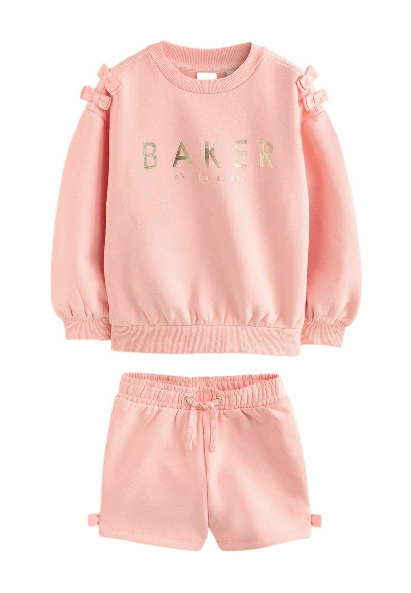 Roosa sviiter ja sobivad lühikesed püksid. Sviiteril on kuldne "BAKER" logo ja paelte aksessuaarid varrukatel. Pehme kangas ja elastsed mansetid.