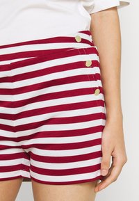 Červeno-bílé pruhované šortky z bavlněné směsi, s třemi zlatými knoflíky na přední straně a přiléhavým střihem.