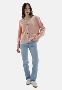 Rosa stickad cardigan med V-ringning, knappstängning och ribbad mudd, ihopparad med ljusblå jeans och vita sneakers.