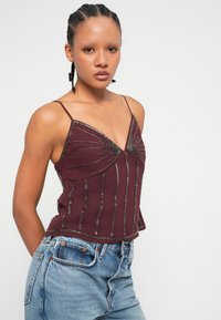 Burgundska majica na naramenice s tankim trakama, s vertikalnimi srebrnimi črtami in v-izrezom, izdelana iz gladkega materiala z rahlim leskom.