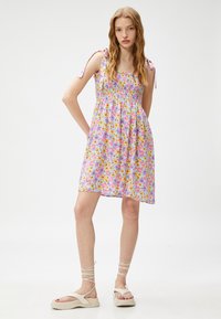 Vestido de estampado floral con torso fruncido, fondo lavanda y tirantes ajustables; combinado con sandalias de plataforma de color claro.