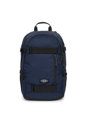 Sac à dos Eastpak bleu marine avec sangles noires, poche avant zippée et poignée supérieure sur fond blanc.