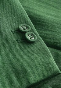 Gros plan sur une manche en tissu vert avec deux boutons recouverts de tissu vert assortis cousus à côté des boutonnières.