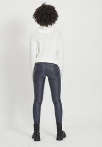 Suéter blanco de punto con cuello alto. Pantalones de imitación cuero azul marino ajustados con costuras visibles y dos bolsillos traseros. Botas negras hasta el tobillo.