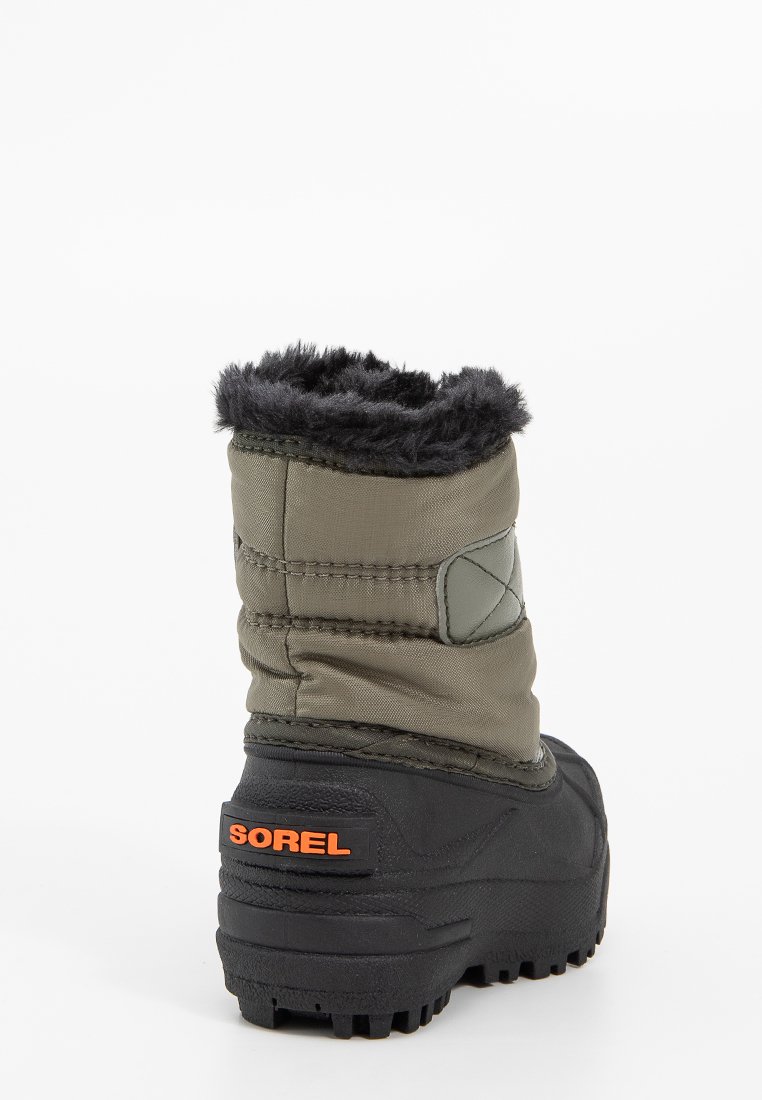 Grüner isolierter Stiefel mit einer schwarzen Gummisohle, Kunstfellfutter an der Oberseite und einem orangefarbenen "SOREL"-Logo an der Ferse. Genähte Designdetails.