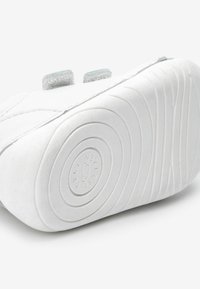 Weiße Sneakers mit einem glatten Lederobermaterial, ausgestattet mit zwei grauen Klettverschlüssen und einer strukturierten Gummisohle mit kreisförmigen Profilmustern.
