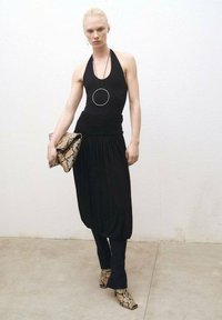 Črn halter bodysuit v kombinaciji s črno drapirano krilo in oprijetimi hlačami. Dodatki vključujejo veliko okroglo ogrlico in torbico z vzorcem kače.