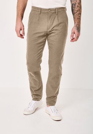 Man wearing beige corduroy pants and white sneakers, standing with hands relaxed by sides against plain background.