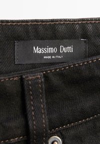 Czarny denim z brązowym przeszyciem; posiada metkę z napisem "Massimo Dutti" i "Made in Italy". Widoczne metalowe elementy.