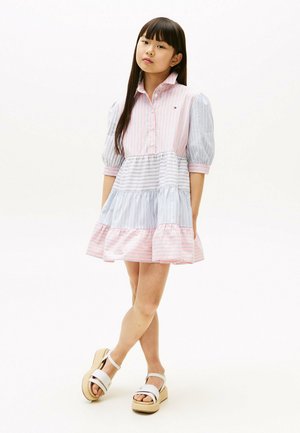 Gestreiftes Kleid mit rosa und hellblauen Paneelen, Kragen, Puffärmeln und Rüsche am Saum. Getragen mit weißen Plateausandalen.