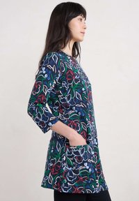 Marineblaues Blumenshirt mit Dreiviertelärmeln, großen Fronttaschen und einem Allover-Druck in roten, grünen und blauen Farbtönen. Weiche Stofftextur.