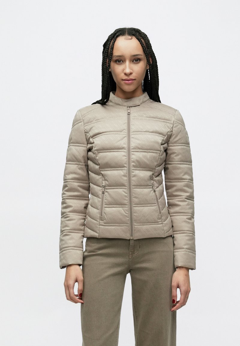 Smėlio spalvos siuvinėta striukė su aukštu apykakliu, dviem priekinėmis užtrauktukų kišenėmis ir lygiu, struktūruotu audiniu. Derinama su siauro kirpimo smėlio spalvos kelnėmis.