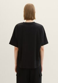 Schwarzes, übergroßes T-Shirt mit kurzen Ärmeln, geripptem Rundhalsausschnitt und geradem Saum, von hinten vor einem hellen Hintergrund gezeigt.