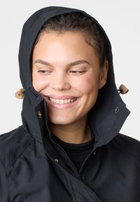 Black waterproof jacket with a high collar and hood. Features a zipper, snap buttons, and leather accents near the neck. Smooth texture.