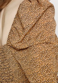 Tissu imprimé léopard en orange et noir, présentant une texture froncée au niveau de la manche et de l'épaule, avec une surface lisse.