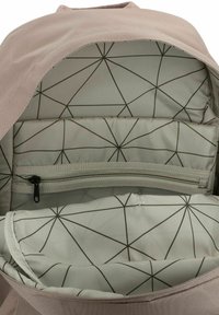 Interior de una mochila marrón claro con un forro de patrón geométrico, compartimentos acolchados, bolsillo con cremallera y una textura de tela suave.