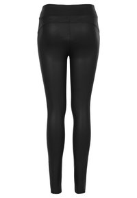 Zwarte leggings van een gladde, rekbare stof, met een hoogtaille ontwerp en zonder zichtbare naden of logo's aan de achterkant. Volledige lengte.