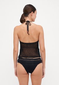Top de bikini negro de ganchillo con diseño de malla abierta, lazos alrededor del cuello y cuentas decorativas. Parte inferior de bikini de tiro alto a juego con acabado texturizado.