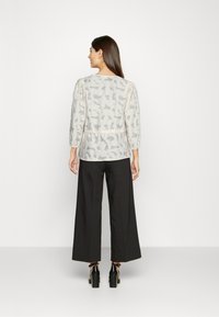 Blusa leve e texturizada de crema com um padrão abstrato cinza, corte descontraído e mangas três-quartos, combinada com calças largas pretas e saltos altos.
