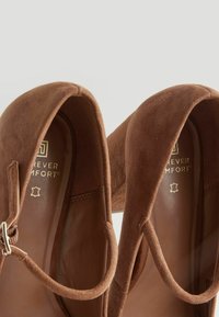 Brown suede slip-on shoes with rounded toe, elasticated straps, and soft inner lining featuring "Forever Comfort" branding.