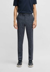 Navy textured trousers with a straight-leg fit, featuring a button closure and side pockets, paired with dark sneakers.