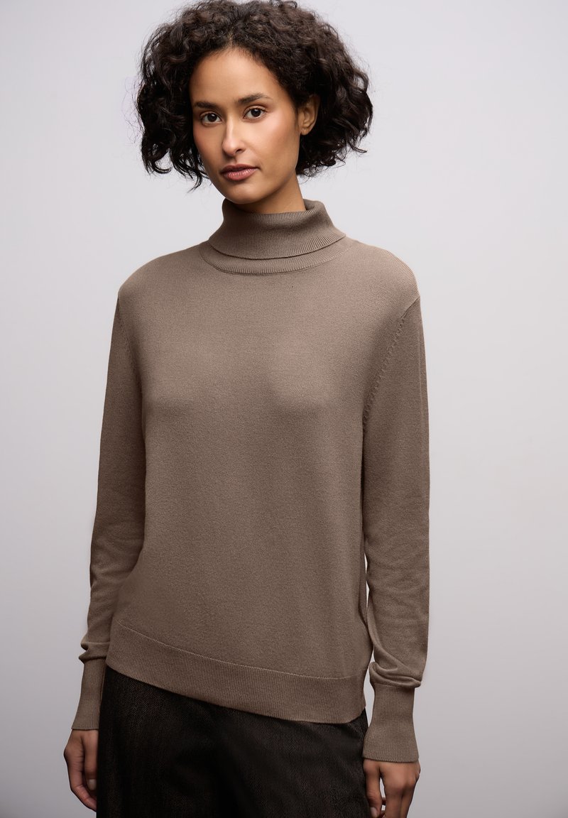 Pull en col roulé marron en tissu doux avec des manches longues, ajusté aux poignets et un ourlet asymétrique pour une silhouette décontractée.