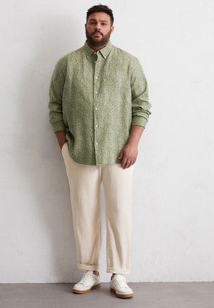 Grün gemusterte Hemdbluse, hellfarbene lässige Hose und weiße Sneaker. Merkmale sind eine weiche Textur und eine lockere Passform.