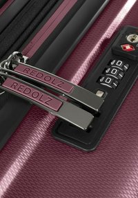 Valigia texturizzata color bordeaux con due zip in metallo contrassegnate "REDOLZ" bloccate da una combinazione nera.
