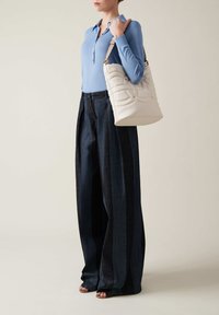 Top azzurro chiaro a maniche lunghe, pantaloni larghi in denim scuro con strisce verticali, borsa a tracolla bianca trapuntata con hardware dorato, sandali beige con cinturini.