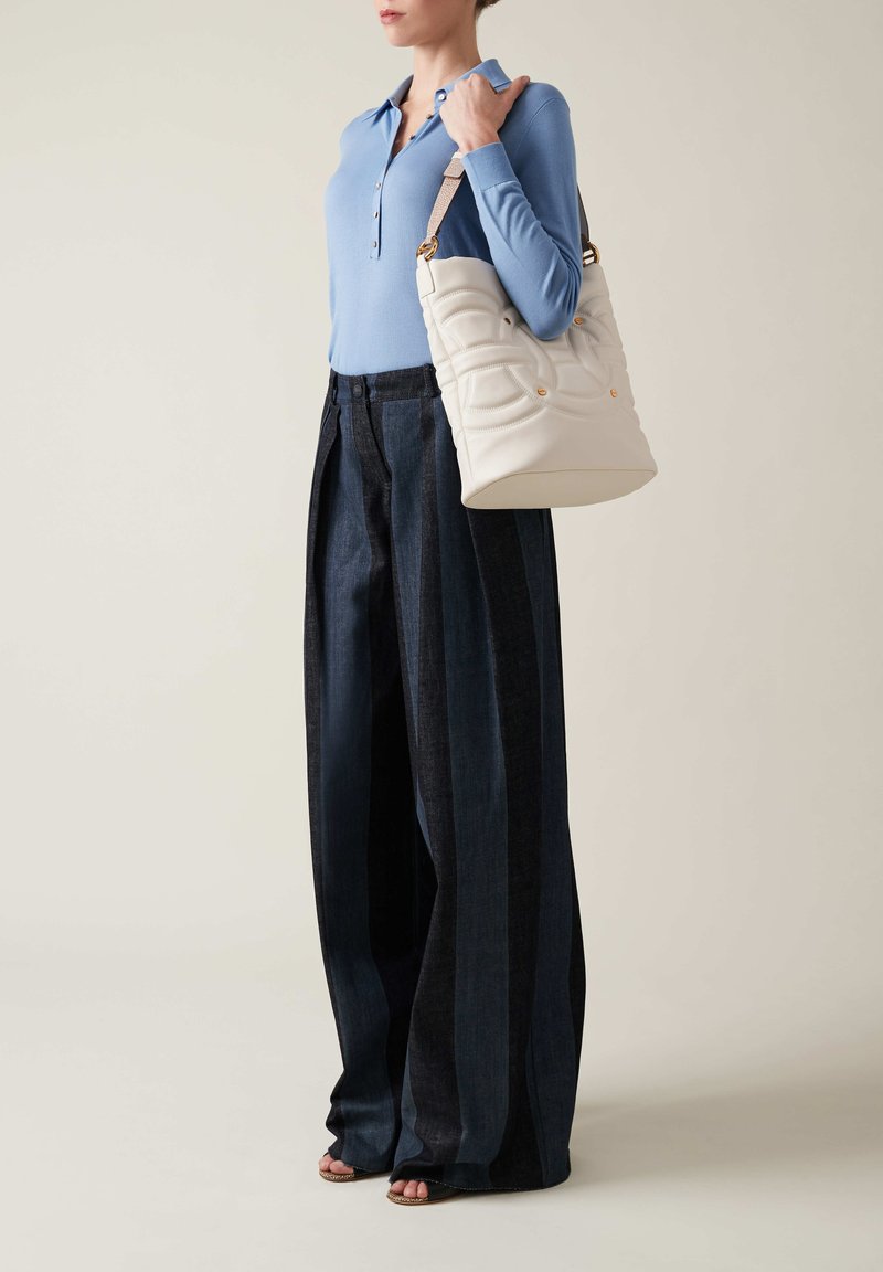 Top azzurro chiaro a maniche lunghe, pantaloni larghi in denim scuro con strisce verticali, borsa a tracolla bianca trapuntata con hardware dorato, sandali beige con cinturini.