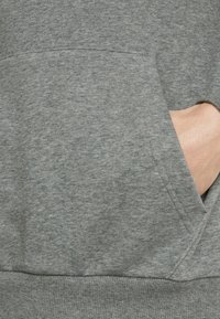 Grijze sweatshirt met een ribbelzoom, textuurstof en een voorzak met een zichtbare hand. Het ontwerp is eenvoudig en casual.