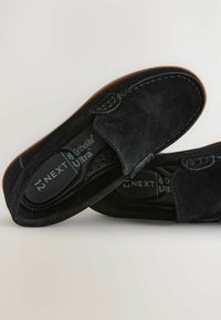 Mocassins en daim noir avec une texture lisse, dotés d'un motif cousu et d'une semelle en caoutchouc. Semelles Ortholite® Ultra pour le confort.