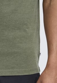 Green short-sleeve shirt made of soft, textured fabric, featuring a curved hem and a small tag on the left side.