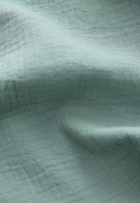 Tissu vert clair et doux avec de légères plis et une surface légèrement texturée et tissée.