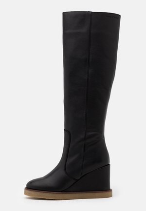 Bottes compensées en cuir noir montant jusqu'au genou, avec un bout arrondi et une texture lisse, présentant un détail de couture subtile le long du côté.