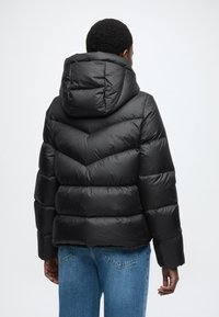 Czarna pikowana kurtka z kapturem, z teksturowanym wzorem w jodełkę i elastycznymi mankietami, w połączeniu z jasnoniebieskimi dżinsami.