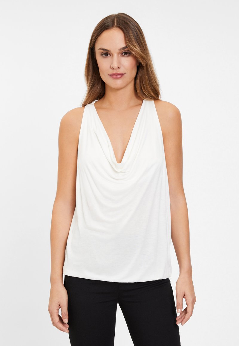 Bílý bezrukávový top s volným dekoltem a měkkou tkaninou. Má volnější střih a hladkou strukturu, stylizovaný s černými upnutými kalhotami.