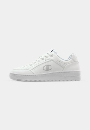 Baskets blanches en cuir avec une texture lisse, bout arrondi, détails perforés et un logo discret sur le côté. Semelle en caoutchouc épaisse.