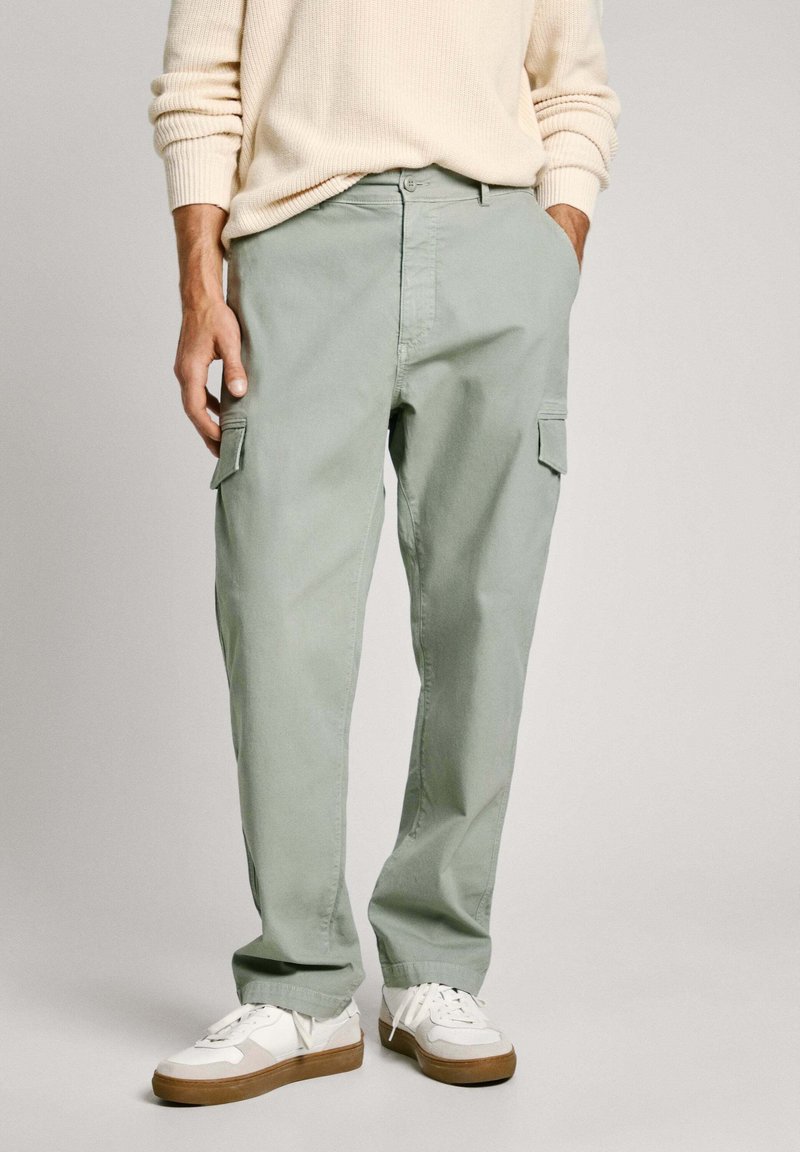 Svetlozeleni cargo hlače iz bombaža, z dvema stranskima žepoma, sproščenim krojem in odprtimi konci, v kombinaciji z belimi športnimi copati.