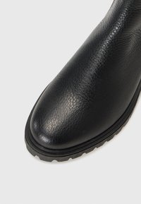 Bota de cuero negra hasta el tobillo con un acabado texturizado, punta redondeada y suela de goma estriada para mayor tracción. Diseño limpio sin adornos.